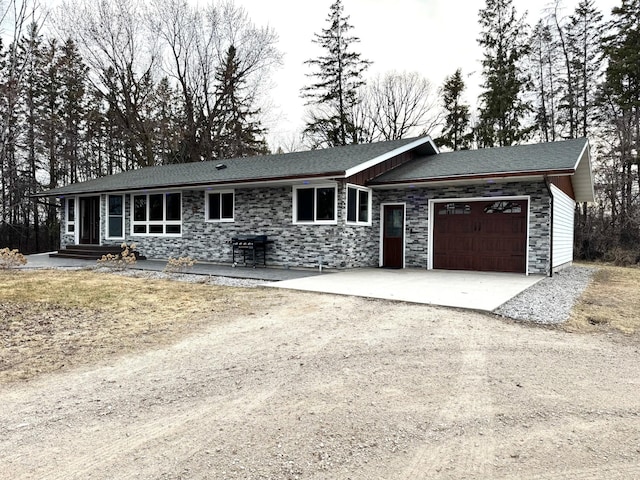 single story home with concrete driveway, an attached garage, roof with shingles, and stone siding