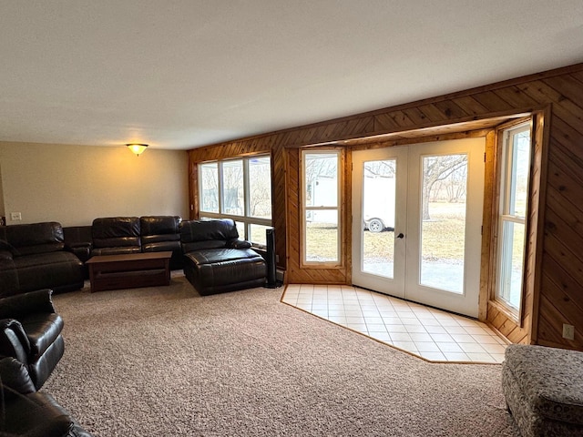 living area featuring light carpet, french doors, wooden walls, and light tile patterned flooring