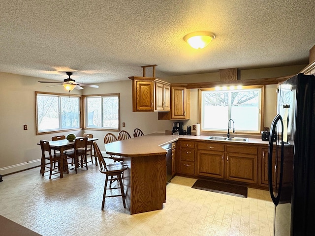 kitchen with a sink, brown cabinets, a kitchen bar, a peninsula, and freestanding refrigerator