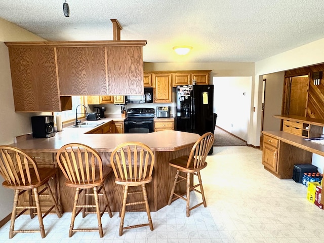 kitchen with black appliances, a peninsula, a sink, and baseboards