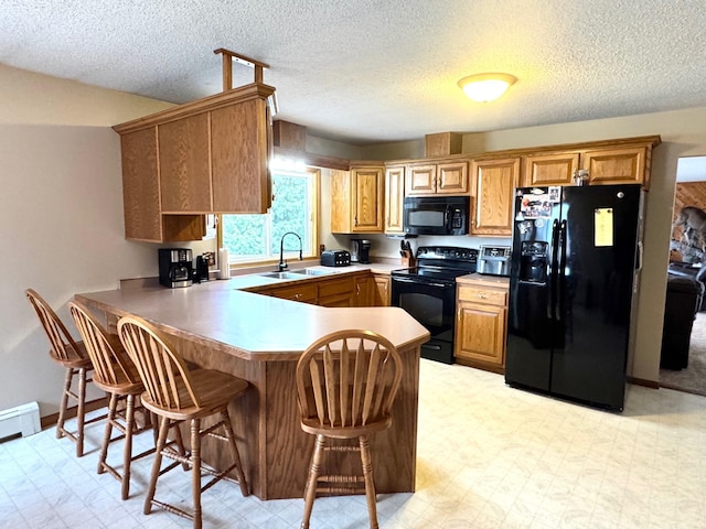 kitchen with light floors, a breakfast bar, a sink, black appliances, and a peninsula
