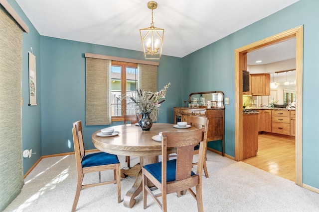 dining space featuring light carpet, a chandelier, and baseboards