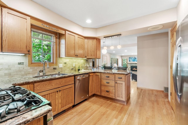 kitchen with appliances with stainless steel finishes, a peninsula, a sink, light wood-type flooring, and backsplash