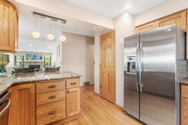 kitchen featuring stainless steel appliances, light wood-style floors, light stone countertops, a fireplace, and pendant lighting