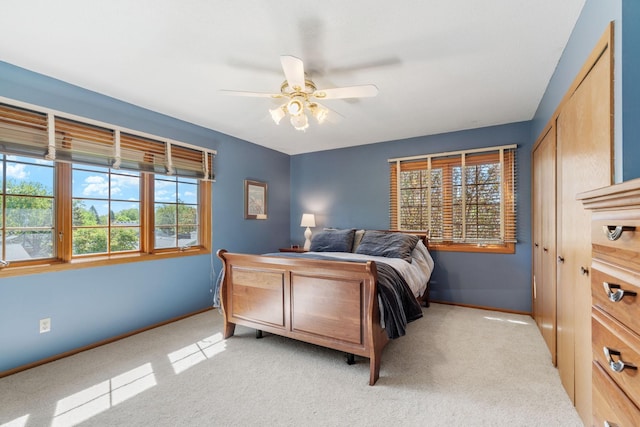 bedroom with baseboards, light colored carpet, a closet, and a ceiling fan