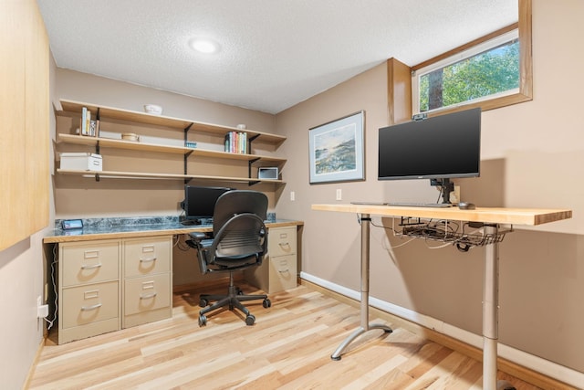 home office featuring a textured ceiling, light wood-style floors, baseboards, and built in study area