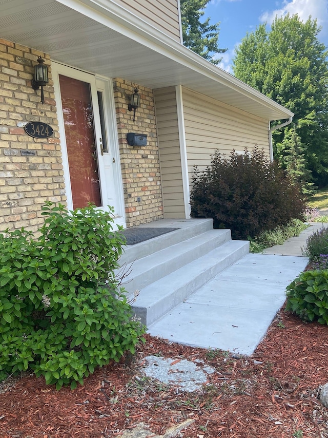 doorway to property featuring a porch and brick siding