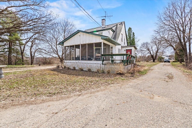 view of front of property featuring dirt driveway, a chimney, and a sunroom