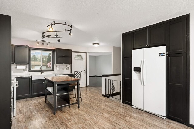 kitchen featuring a sink, light countertops, white fridge with ice dispenser, and light wood-style flooring