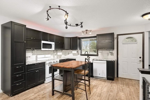 kitchen featuring dark cabinets, tasteful backsplash, white appliances, and light wood-type flooring