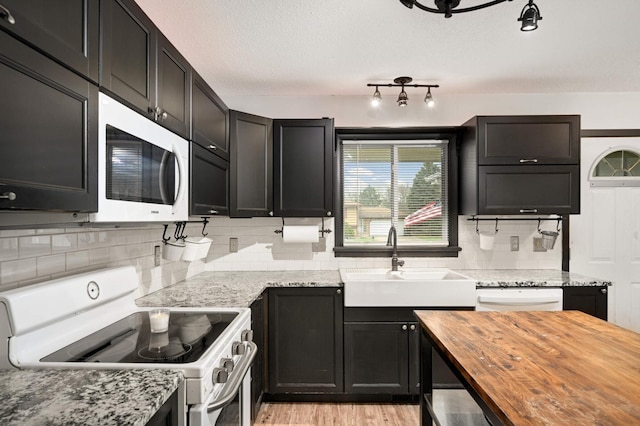 kitchen with wood counters, dark cabinetry, backsplash, and white appliances