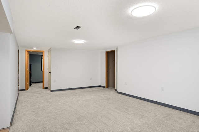spare room featuring a textured ceiling, light colored carpet, and baseboards