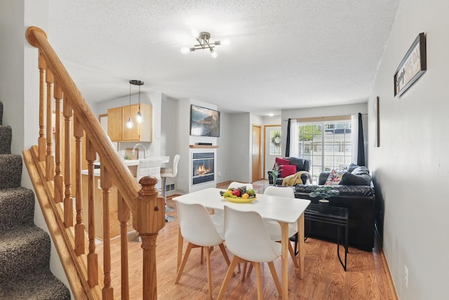 8397 Corcoran Cir Unit 26, Inver Grove Heights, MN 55076 - dining room featuring a textured ceiling, light wood-style floors, stairway, a glass covered fireplace, and baseboards