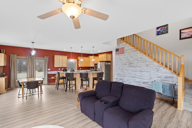 living room featuring light wood-type flooring, a ceiling fan, and stairs