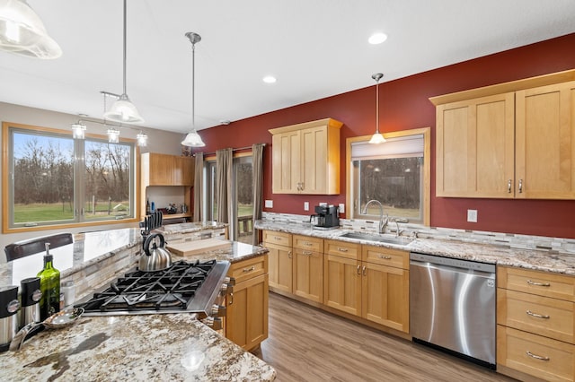 kitchen with stainless steel dishwasher, light brown cabinetry, light wood-style floors, a sink, and pendant lighting
