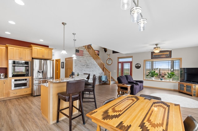 kitchen with stainless steel refrigerator with ice dispenser, a kitchen bar, light brown cabinets, and light wood finished floors