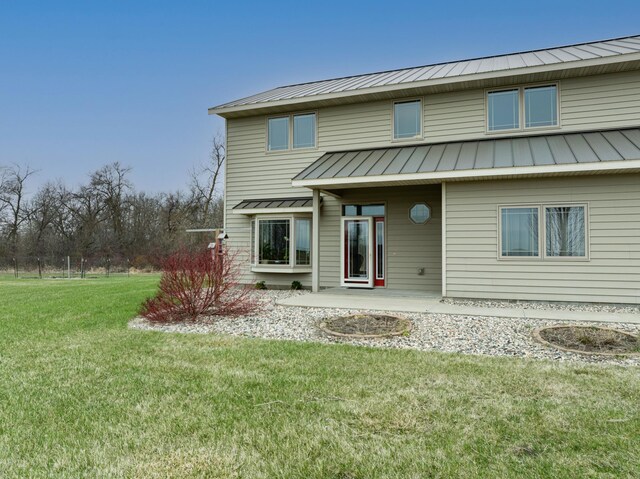 rear view of property featuring a lawn, a standing seam roof, metal roof, and a patio area