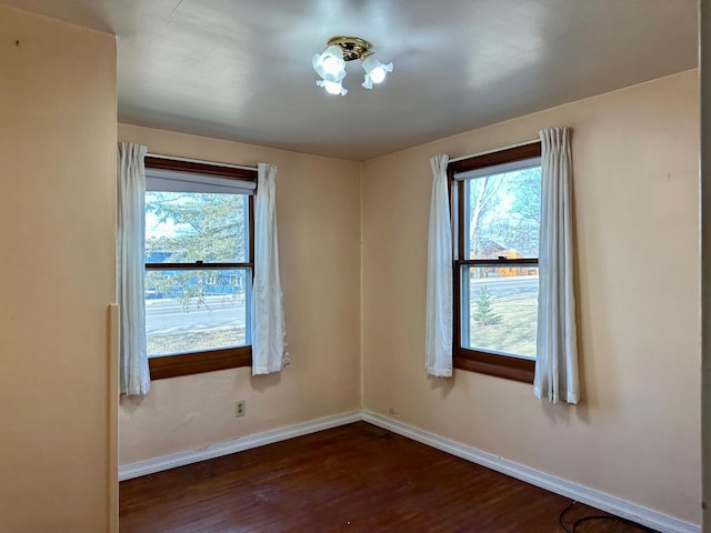 spare room with dark wood-style flooring, baseboards, and healthy amount of natural light
