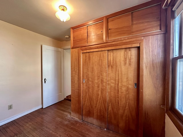unfurnished bedroom with dark wood-style floors, baseboards, a closet, and multiple windows
