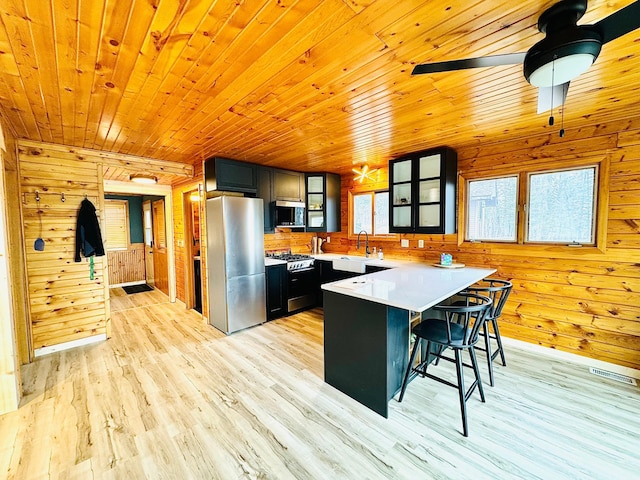 41820 Bald Eagle Dr, Marcell Twp, MN 56628 - kitchen featuring appliances with stainless steel finishes, a peninsula, wooden walls, light wood-style floors, and a breakfast bar area