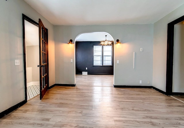 423 1st St NW, Faribault, MN 55021 - empty room with arched walkways, light wood-style floors, a chandelier, and baseboards