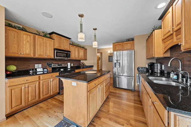 kitchen featuring appliances with stainless steel finishes, a sink, a center island, light wood-style flooring, and tasteful backsplash