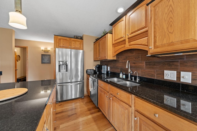 kitchen featuring appliances with stainless steel finishes, a sink, tasteful backsplash, dark stone countertops, and light wood-type flooring