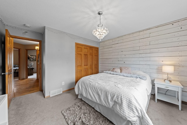 carpeted bedroom featuring a chandelier, a closet, wooden walls, and baseboards