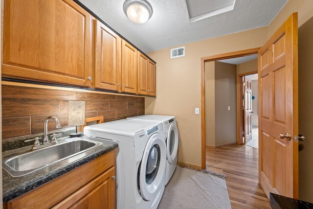laundry area with cabinet space, washing machine and dryer, a textured ceiling, light wood-style floors, and baseboards