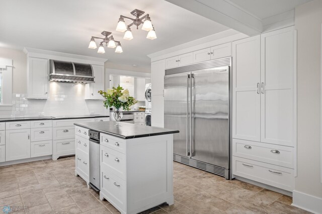 9730 177th Ave SE, Fairmount, ND 58030 - kitchen with dark countertops, built in fridge, white cabinets, wall chimney exhaust hood, and stacked washer and dryer