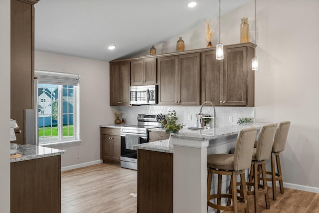 5928 Th St W, Lakeville, MN 55044 - kitchen featuring appliances with stainless steel finishes, tasteful backsplash, a peninsula, lofted ceiling, and light wood-type flooring