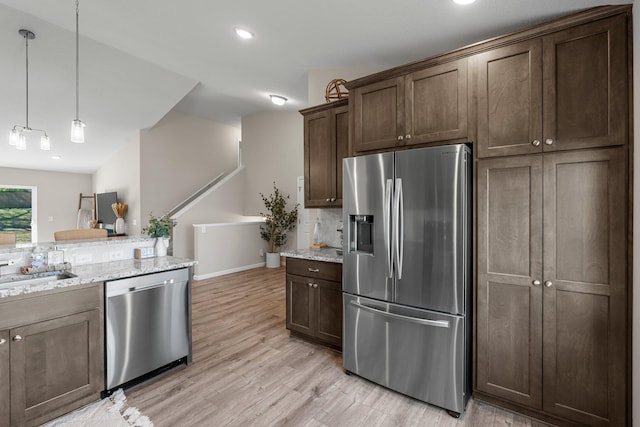 5928 Th St W, Lakeville, MN 55044 - kitchen featuring appliances with stainless steel finishes, dark brown cabinetry, light wood-style flooring, light stone countertops, and decorative light fixtures