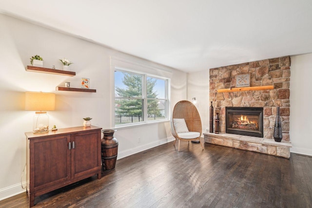 living area with wood finished floors, baseboards, and a stone fireplace