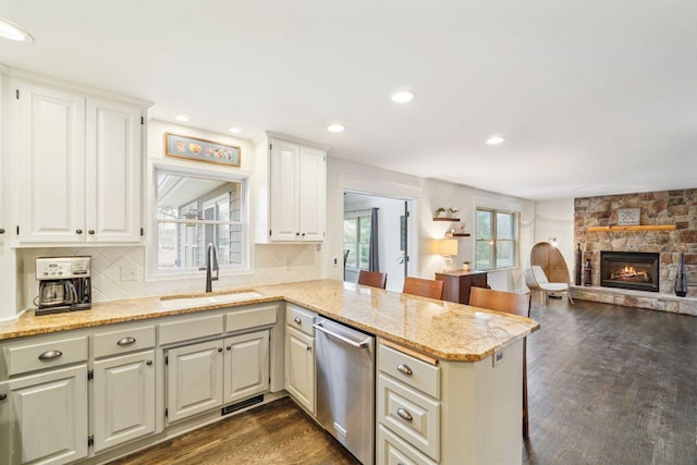 kitchen featuring a peninsula, a sink, light stone counters, dishwasher, and dark wood-type flooring