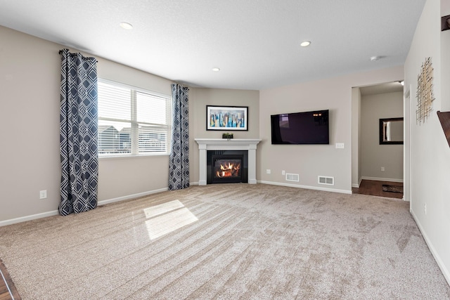 unfurnished living room featuring recessed lighting, a glass covered fireplace, visible vents, and carpet flooring
