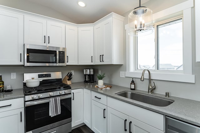kitchen featuring vaulted ceiling, a sink, stainless steel appliances, decorative light fixtures, and white cabinetry