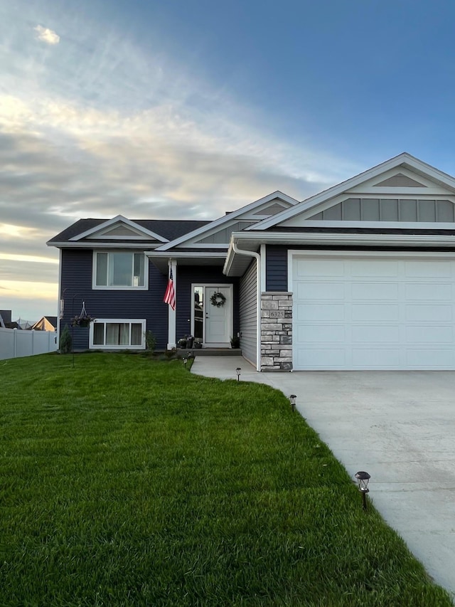 view of front of home featuring a front lawn, driveway, stone siding, fence, and a garage