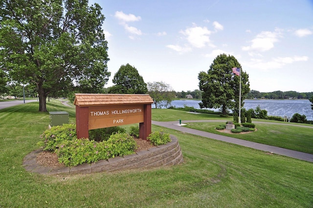 community / neighborhood sign featuring a lawn and a water view