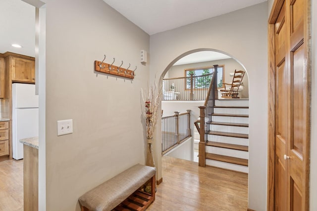 corridor featuring light wood-type flooring, arched walkways, recessed lighting, and stairs