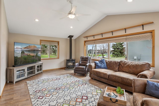 living room with ceiling fan, vaulted ceiling, wood finished floors, and a wood stove