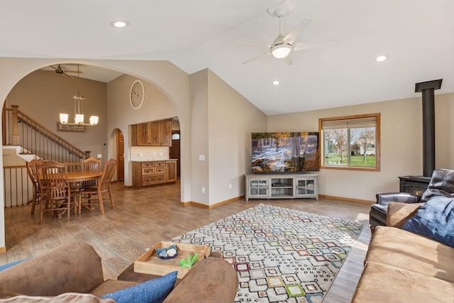 living area featuring light wood finished floors, arched walkways, vaulted ceiling, ceiling fan with notable chandelier, and a wood stove