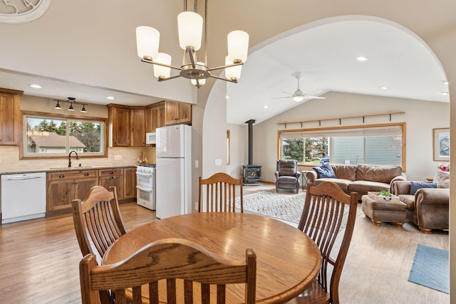 dining area featuring arched walkways, a wood stove, light wood finished floors, and ceiling fan with notable chandelier