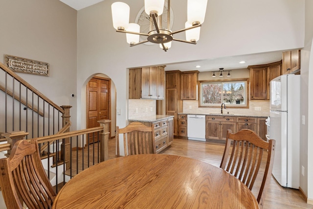 dining space featuring arched walkways, a notable chandelier, stairs, and light wood finished floors