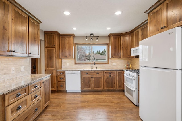 kitchen with brown cabinetry, white appliances, a sink, and backsplash