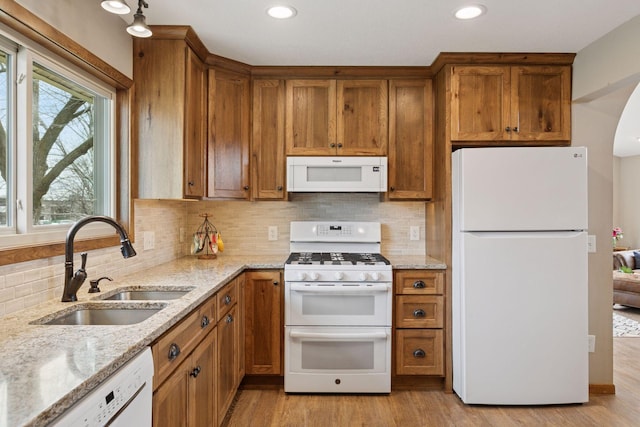 kitchen with brown cabinets, backsplash, a sink, and white appliances