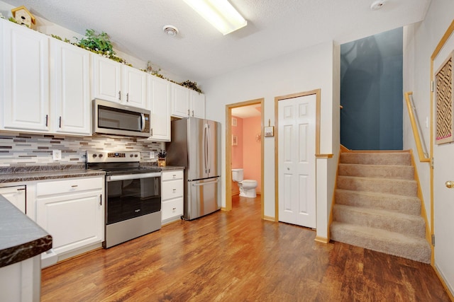 kitchen with wood finished floors, dark countertops, white cabinets, tasteful backsplash, and stainless steel appliances