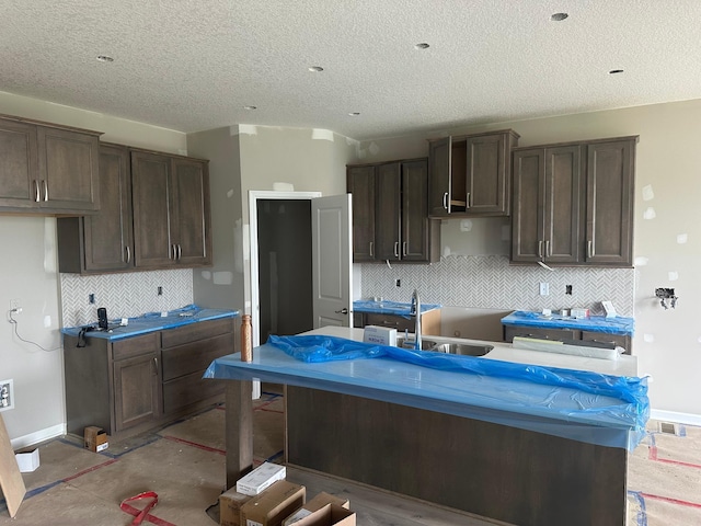 2063 Oakpointe Dr, Waconia, MN 55387 - kitchen featuring backsplash, a textured ceiling, dark brown cabinetry, and an island with sink