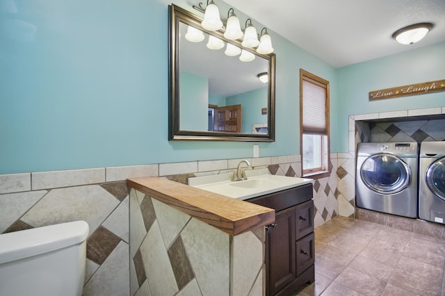 235 3rd St NE, Blooming Prairie, MN 55917 - bathroom with tile patterned floors, a wainscoted wall, toilet, washing machine and dryer, and tile walls
