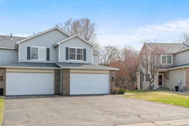 view of front of house with roof with shingles, brick siding, an attached garage, a front yard, and aphalt driveway