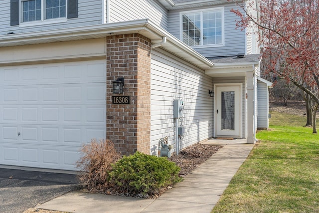 property entrance featuring an attached garage, a lawn, and brick siding